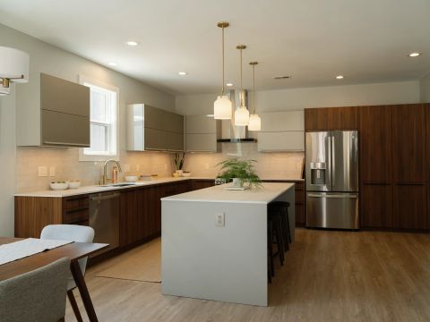 Greenville kitchen with light gray island, dark walnut base cabinets, taupe upper cabinets, white quartz countertops, gold pendant lights, brass faucet, and stainless steel refrigerator by Tekton Builds.
