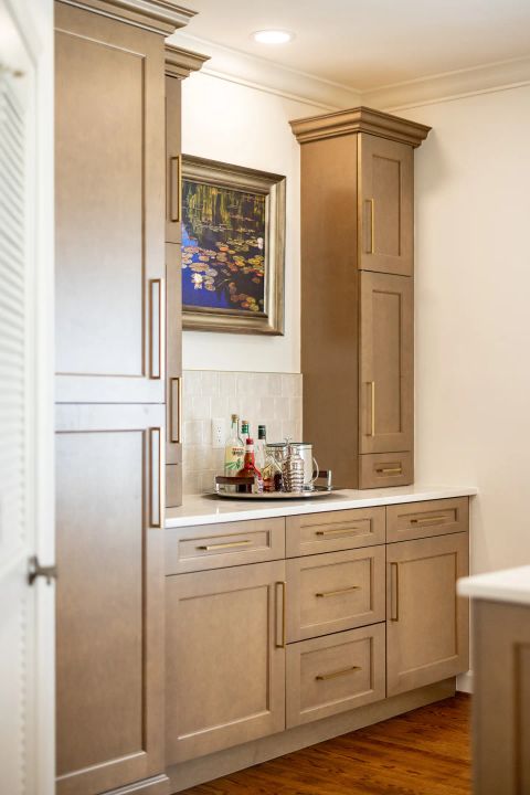 Greenville wet bar with light brown wood cabinetry, brushed gold bar pulls, white quartz countertops, subway tile backsplash, and water lily painting by Tekton Builds.