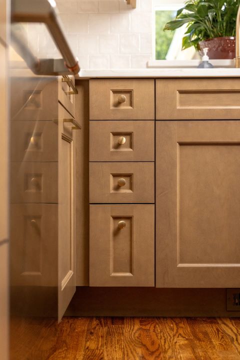 Greenville kitchen with light-toned wood cabinetry, recessed panel design, brass knobs, white countertop and backsplash, and hardwood flooring by Tekton Builds.