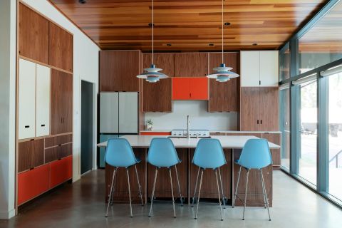 Greenville mid-century modern kitchen with walnut cabinetry, orange accents, white island with blue bar stools, and wood-paneled ceiling by Tekton Builds.