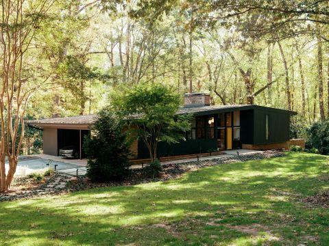 Greenville modern home exterior with dark charcoal facade, vibrant yellow front door, large windows, carport, and stone path by Tekton Builds.