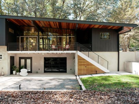 Greenville two-story home with dark grey upper facade, light concrete lower level, glass windows, balcony, and black glass garage door by Tekton Builds.