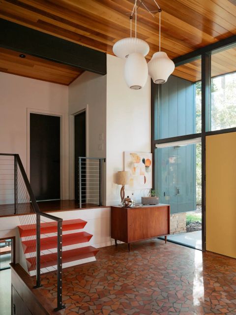 Greenville entryway with red-orange open-riser staircase, black metal railings, wood-paneled ceiling, and mosaic tile floor by Tekton Builds.