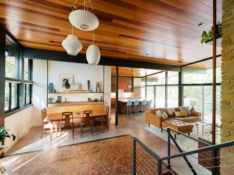 Greenville dining and kitchen with wooden dining table, mid-century modern chairs, built-in bench, polished concrete floors, and orange accent cabinets by Tekton Builds.