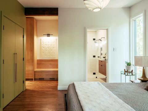 Greenville master bedroom with sage green floor-to-ceiling closet, light-wood cabinetry, built-in bench, and glass shower enclosure by Tekton Builds.